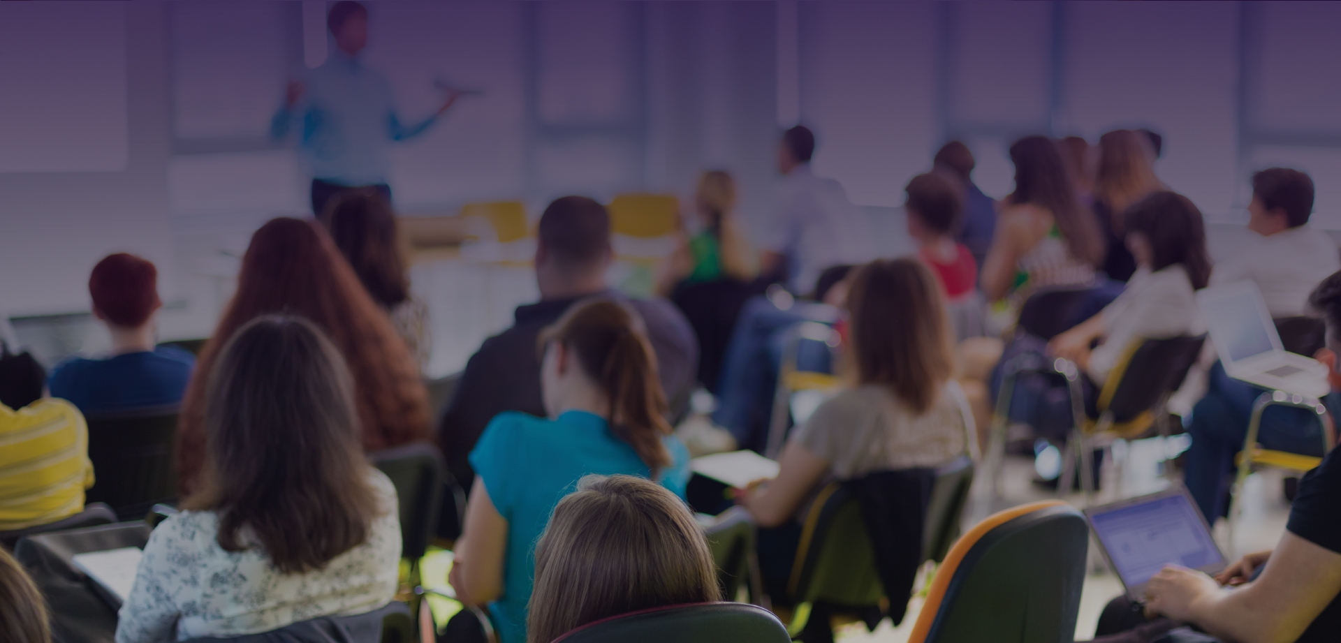 Faded background of a classroom taking notes at desks while listening to an instructor