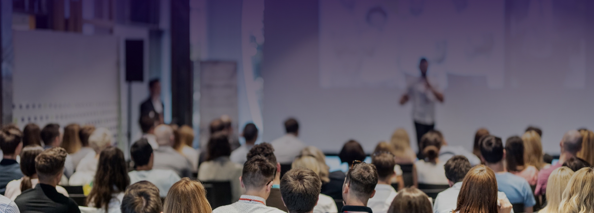 Someone with a microphone speaking to a room full of people at a conference.