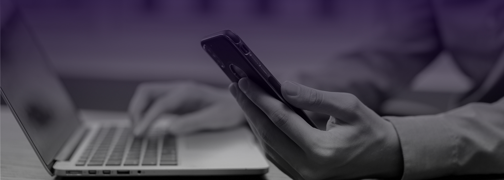 A closeup of someone holding a cell phone and typing on a laptop.