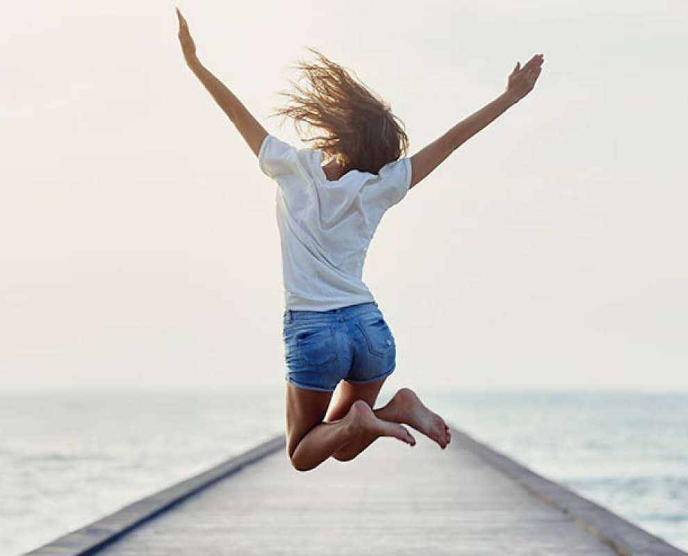 A girl jumping into the air on the dock of a beach.