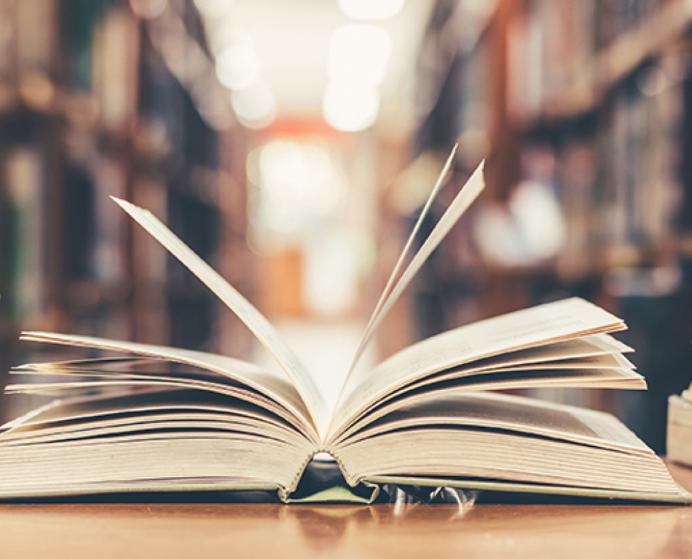 Closeup of an open book with a faded library in the background.