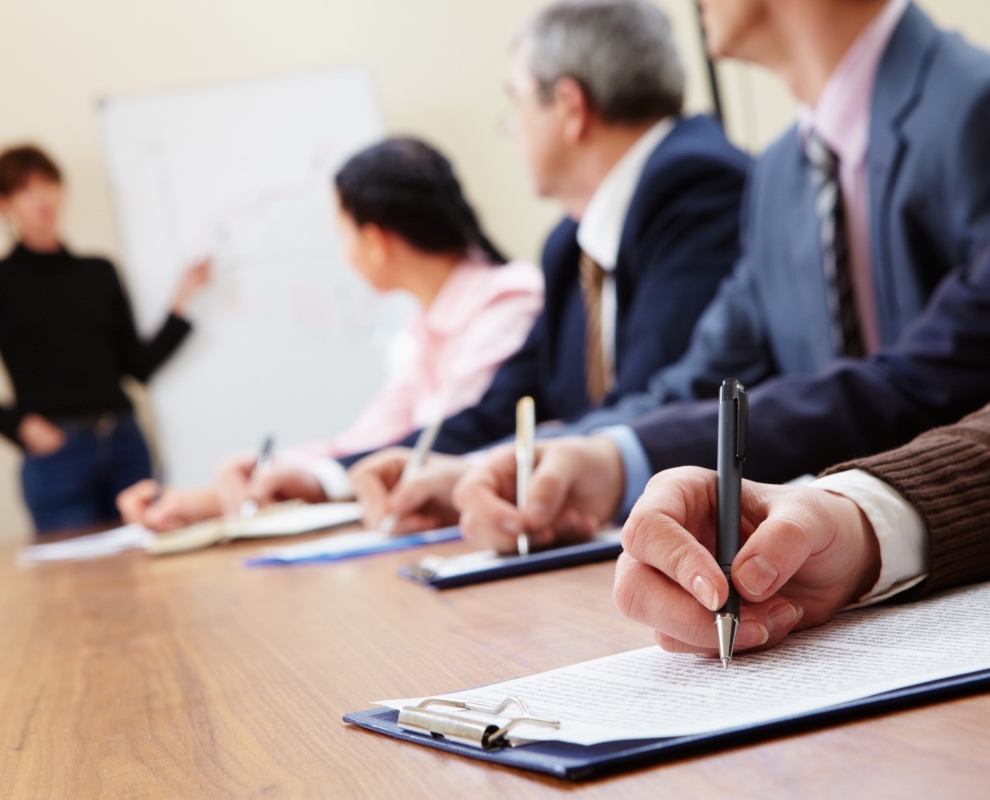 People taking notes in a conference room while listening to a speaker.