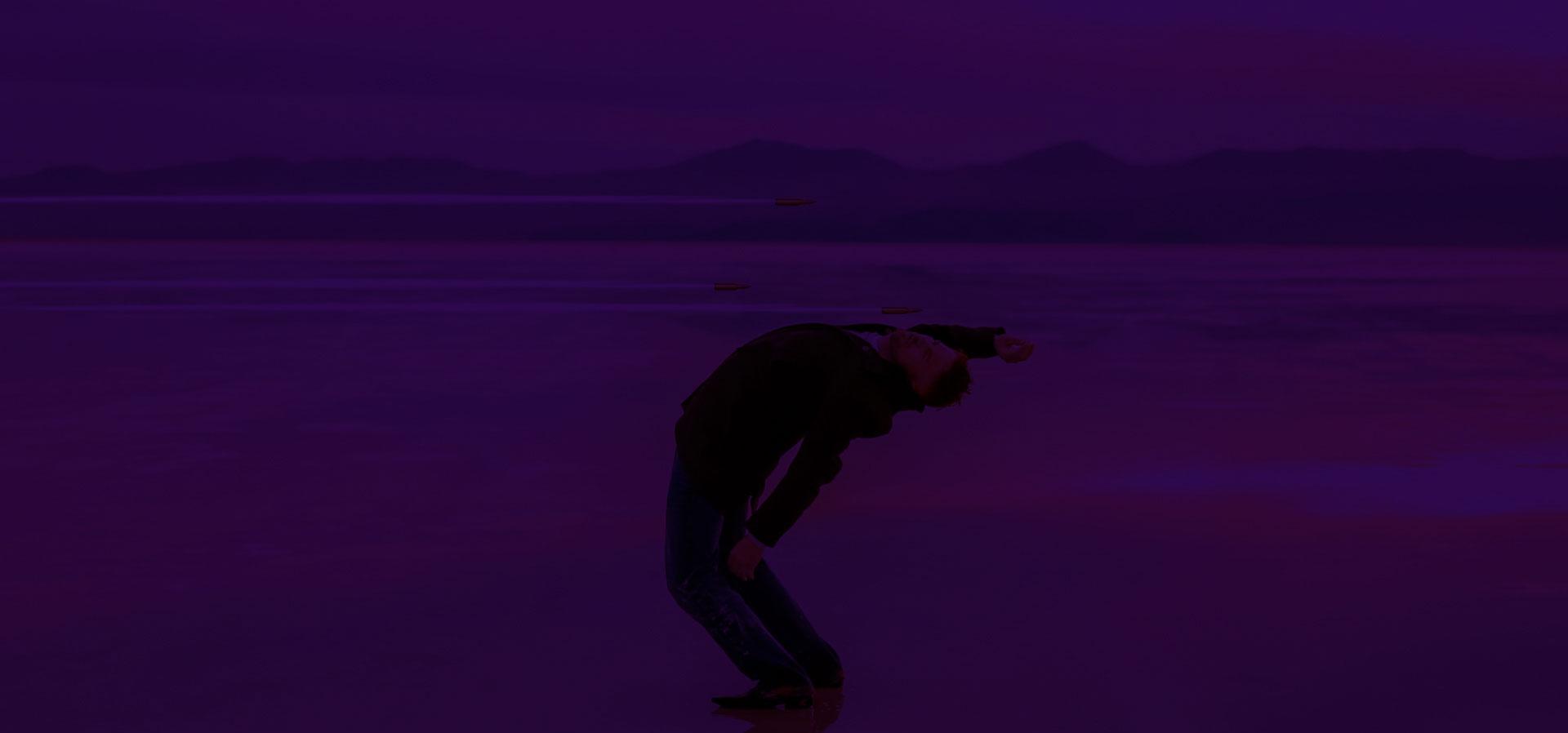 Background Image of Taylor Skinner dodging bullets in front of mountains in the Utah desert.