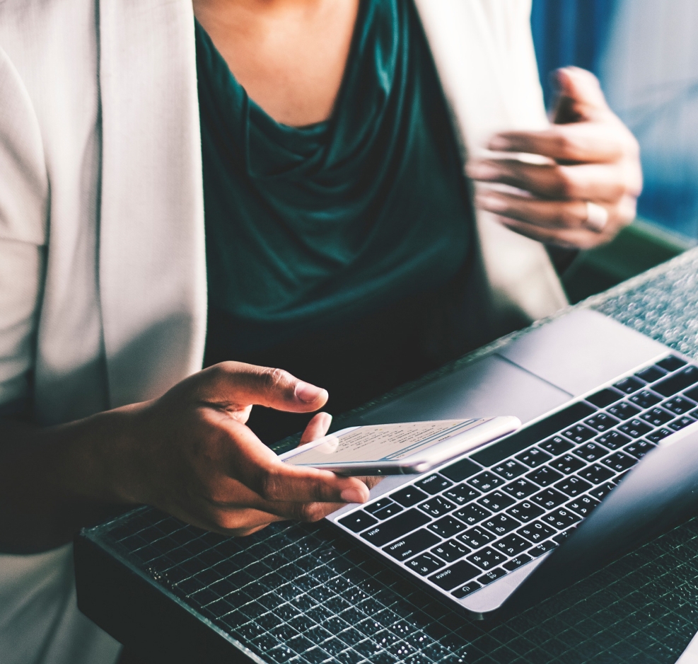 Closeup of a woman holding a cell phone while working on a laptop.